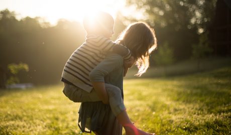 Image of Children - A girl giving a young boy a piggy back with the sun shining in the background